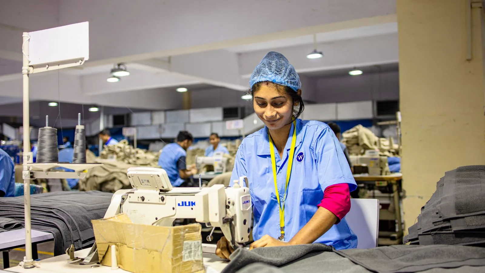 A female textile worker sewing fabric in an industrial factory setting.