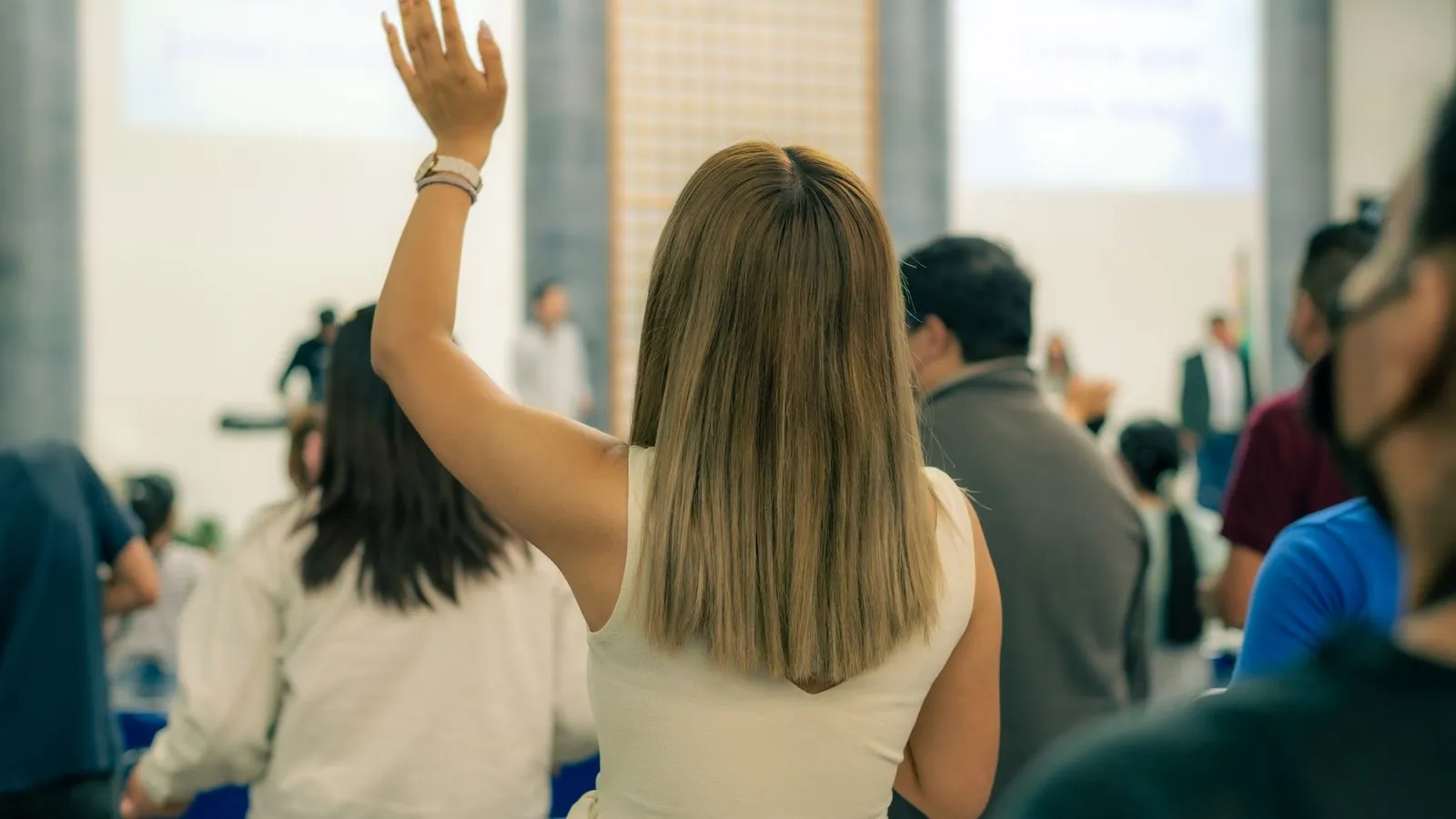 Back view of a woman raising hand during an indoor event, showcasing engagement.
