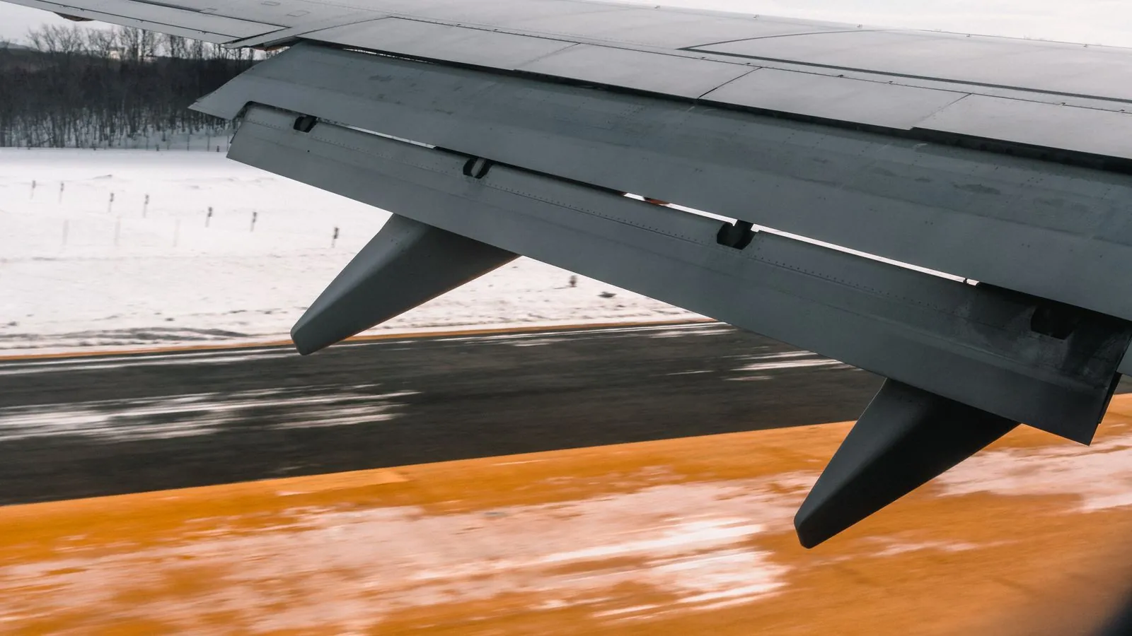 Close-up of an airplane wing during landing on a snowy runway, showcasing aviation dynamics.