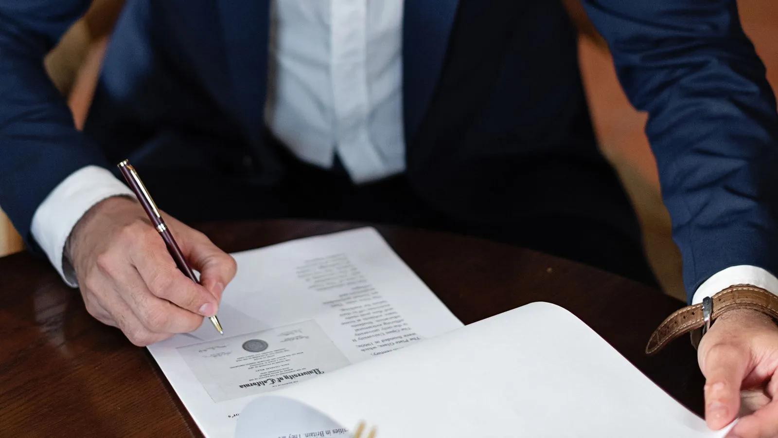 A professional individual signs legal documents at a desk in an office setting.