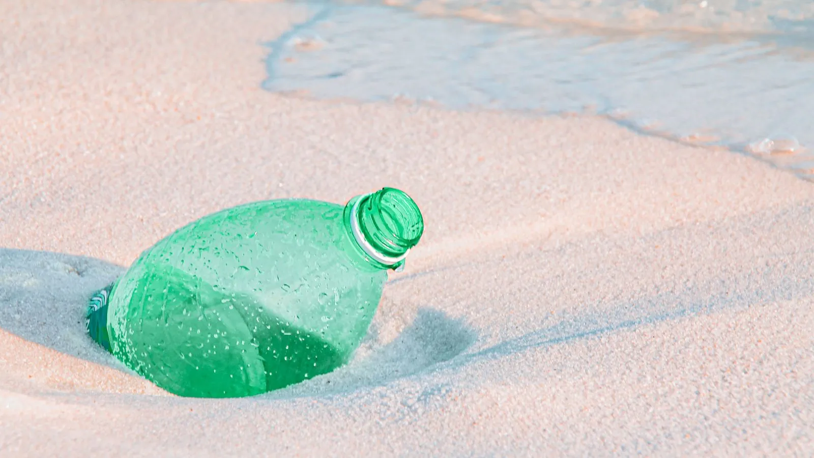 Discarded plastic bottle on the sandy beach illustrating environmental pollution.